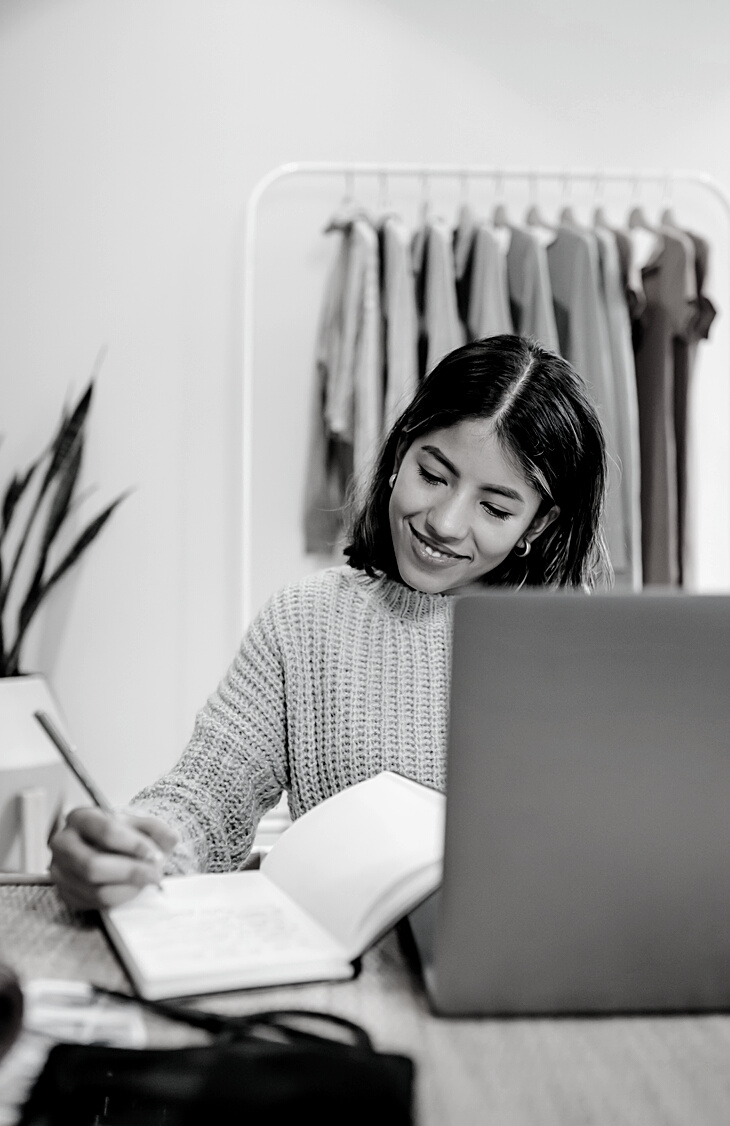 Smiling ethnic employee with diary and laptop at home